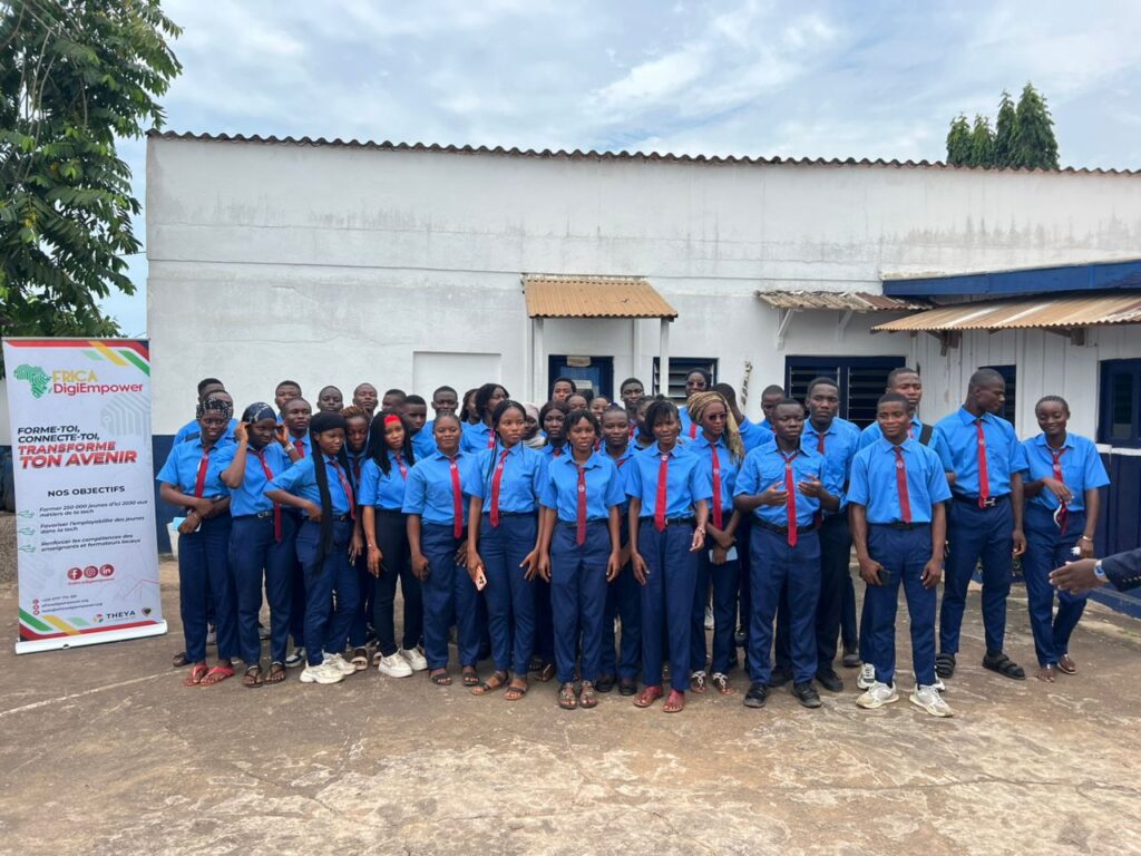 Groupe d'élèves en uniforme bleu et cravate rouge, posant avec plusieurs adultes devant un bâtiment blanc. Dans le cadre de son programme phare Africa DigiEmpower, THEYA by Cybastion a déployé du 24 au 27 mars 2026 une mission de formation d'envergure à San Pedro, formateurs et encadrants a sillonné les établissements de la ville pour offrir des formations gratuites et certifiantes aux étudiants et jeunes de la région-Africa DigiEmpower formations gratuites pour les jeunes. design by adambita237