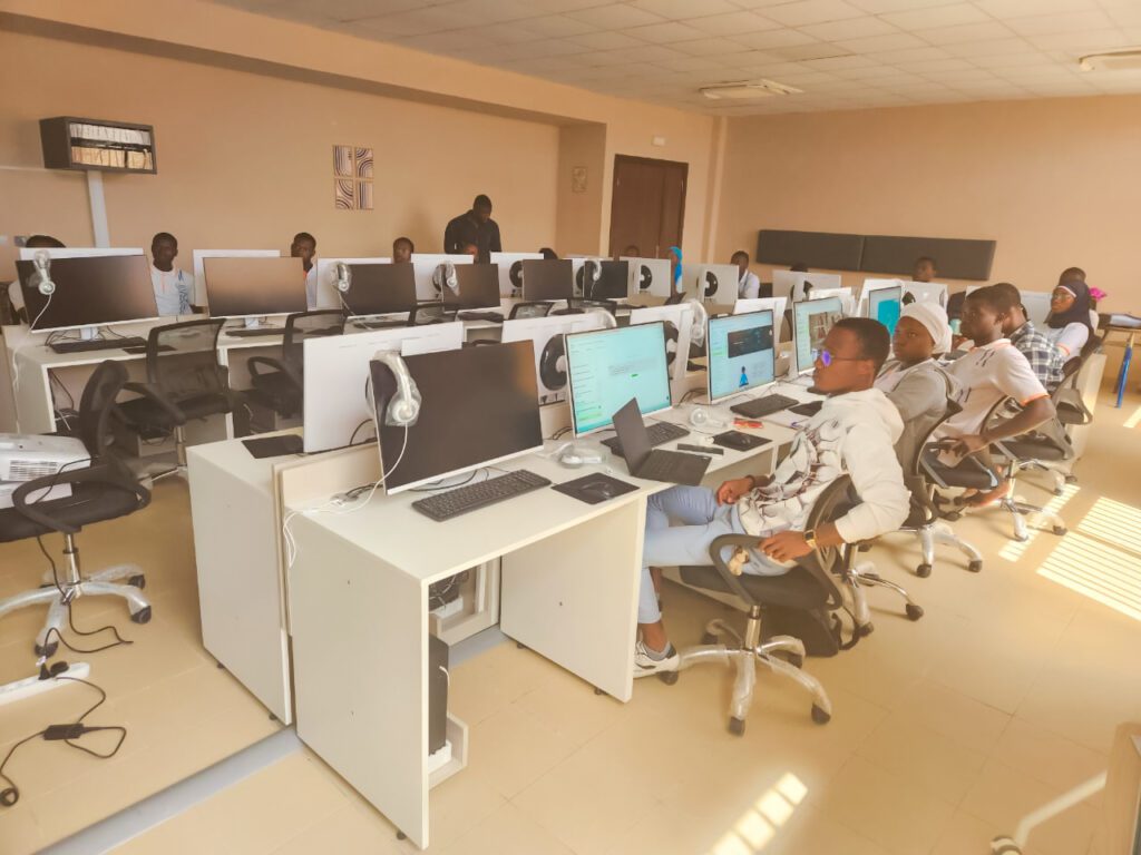 Groupe d'élèves en uniforme bleu et cravate rouge, posant avec plusieurs adultes devant un bâtiment blanc. Dans le cadre de son programme phare Africa DigiEmpower, THEYA by Cybastion a déployé du 24 au 27 mars 2026 une mission de formation d'envergure à San Pedro, formateurs et encadrants a sillonné les établissements de la ville pour offrir des formations gratuites et certifiantes aux étudiants et jeunes de la région-Africa DigiEmpower formations gratuites pour les jeunes. design by adambita237